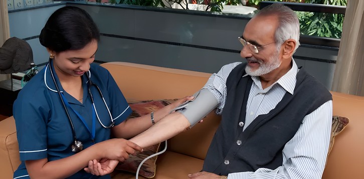 Nurse checking an elderly man's blood pressure on the sofa at home